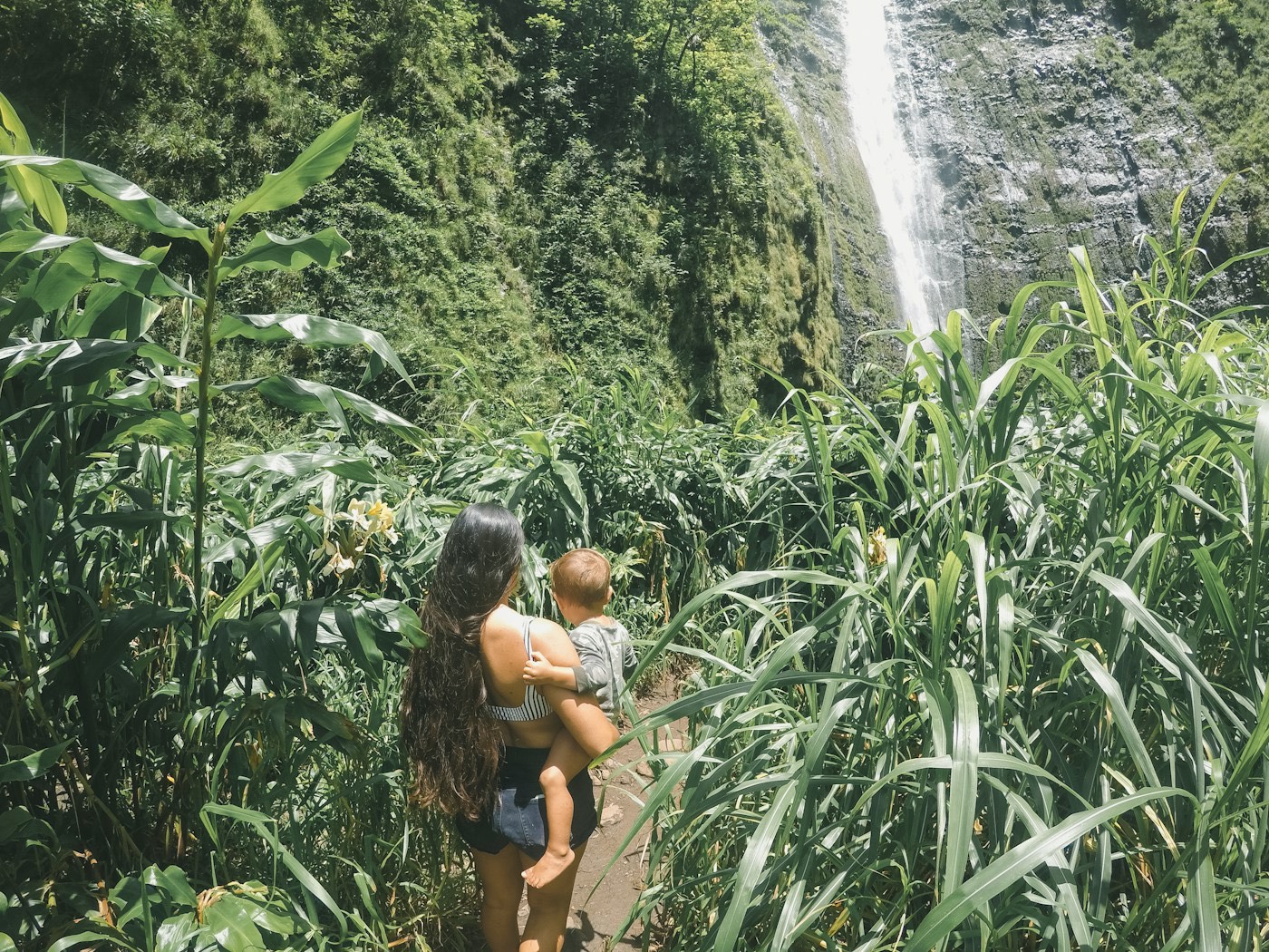Mãe com bebê no colo caminhando em direção a uma cachoeira